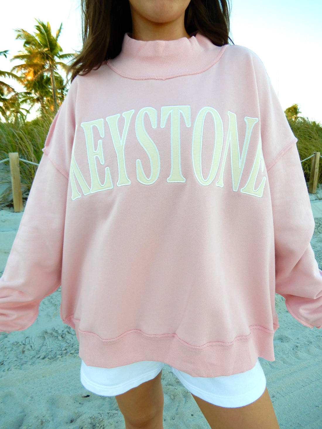 Person wearing a pink sweatshirt with 'Keystone' printed on it at the beach.