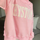 Person wearing a pink hoodie with 'KEYSTONE' printed on it, sitting on a couch.