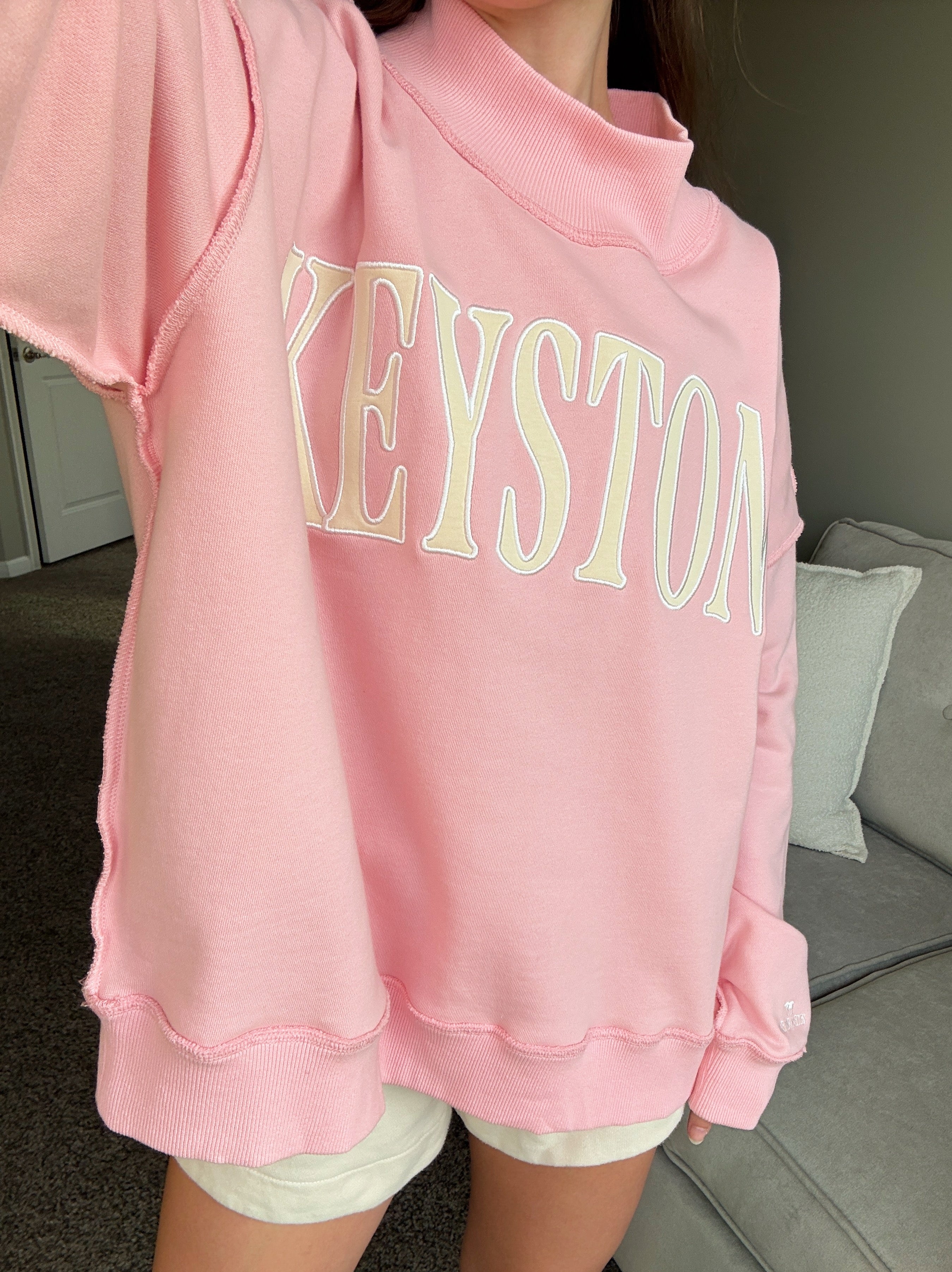 Person wearing a pink hoodie with 'KEYSTONE' printed on it, sitting on a couch.
