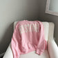 Pink sweatshirt with cream text laying on white chair