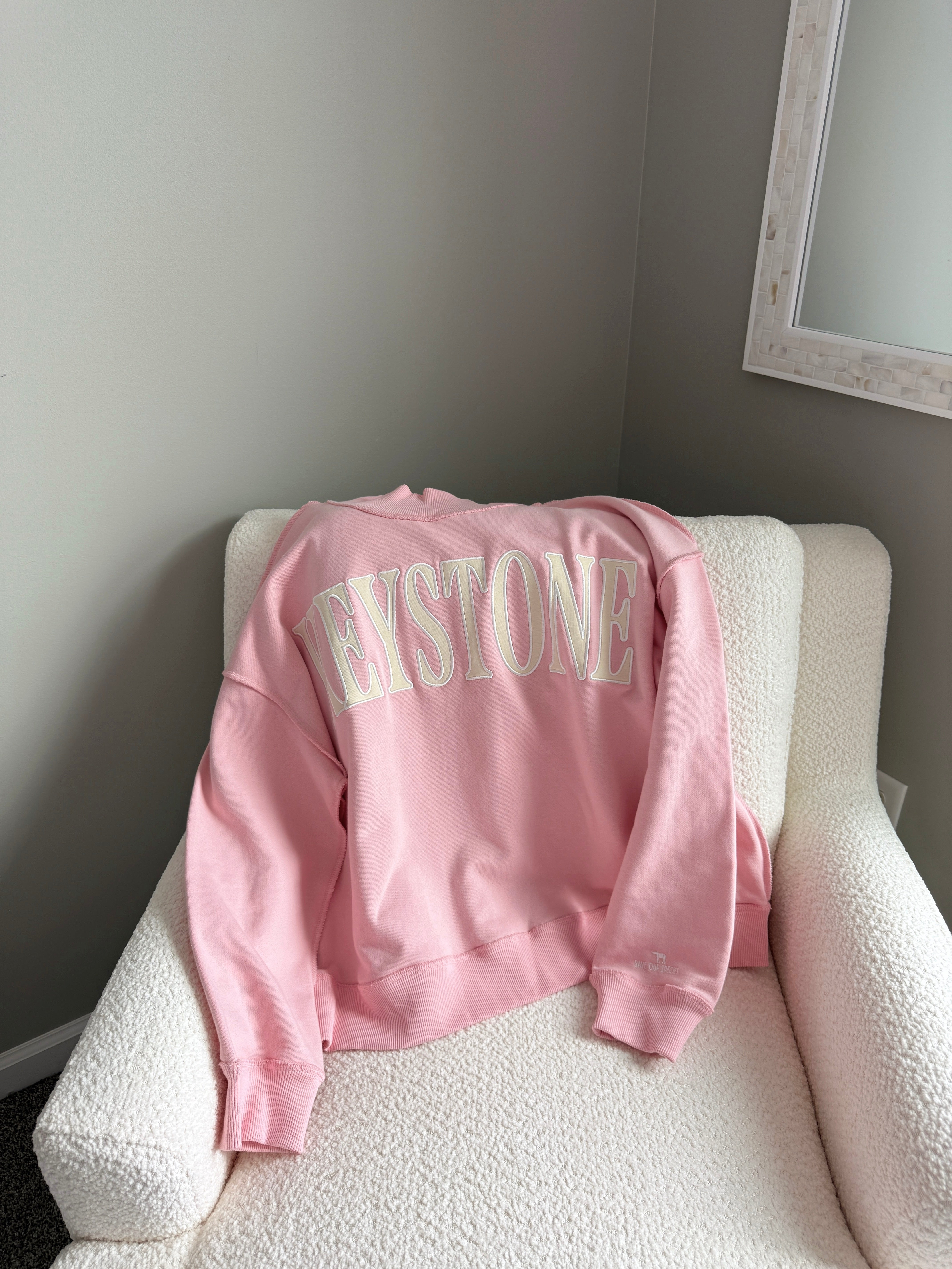 Pink sweatshirt with cream text laying on white chair