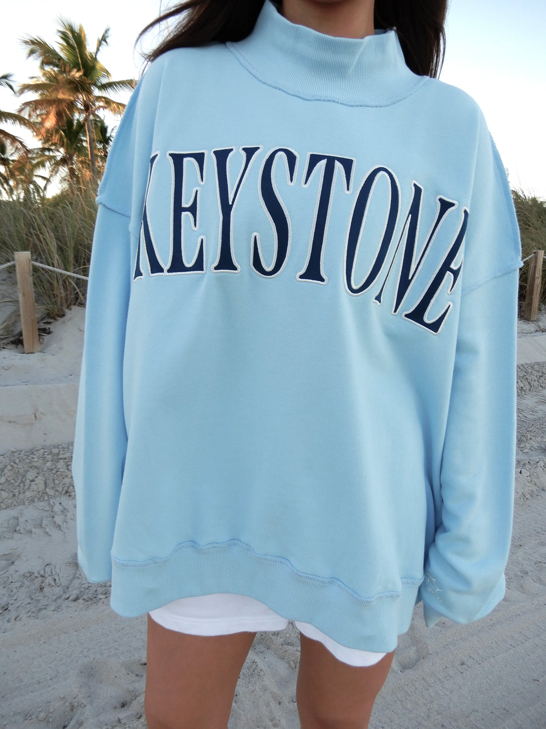 Person wearing a light blue sweatshirt with 'Keystone' text on a beach.
