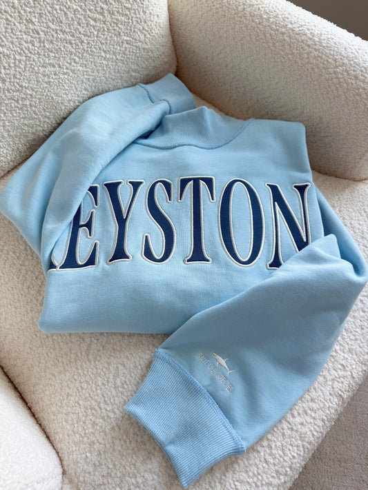 Light blue sweatshirt with 'KEYSTONE' printed on it, laid flat on a beige surface.