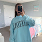 Person wearing a light blue sweatshirt with text in a bedroom setting