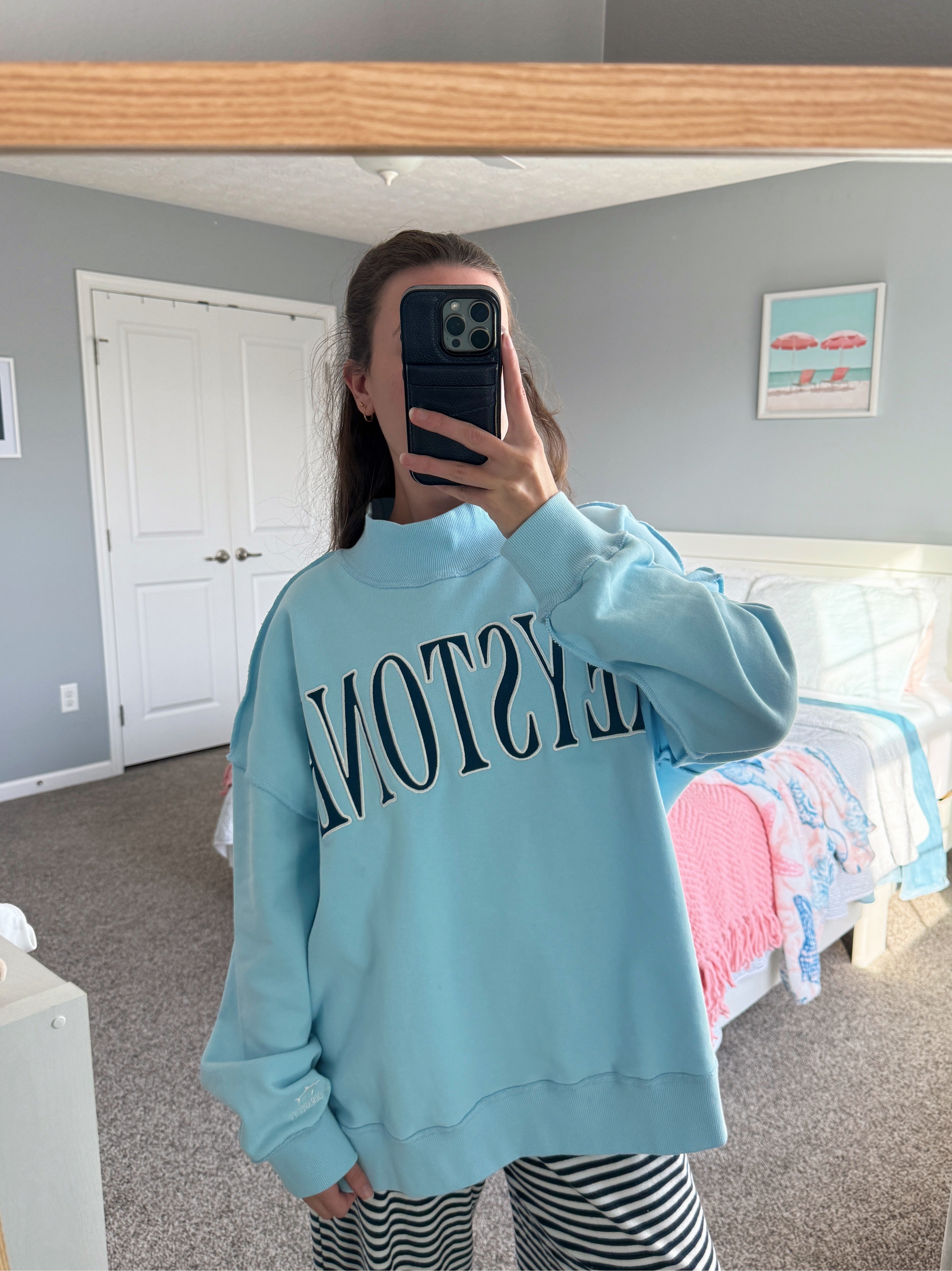 Person wearing a light blue sweatshirt with text in a bedroom setting