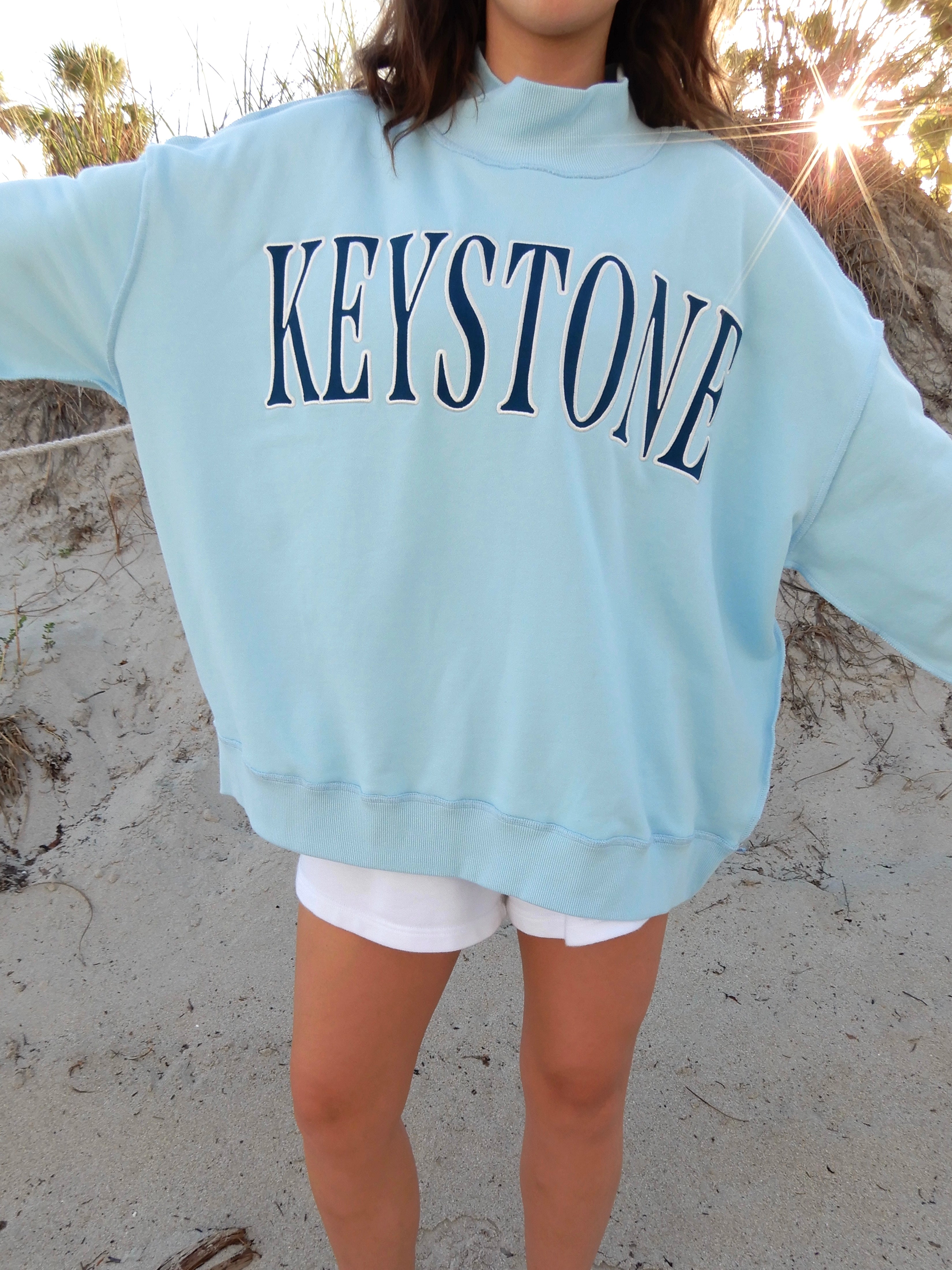 Person wearing a blue sweatshirt with dark 'KEYSTONE' text on a sandy surface