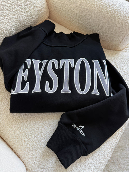 Black sweatshirt with 'KEYSTONE' printed on it, lying on a textured surface.
