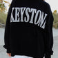 Person wearing a black sweatshirt with 'KESTONE' printed on it, standing on a sandy beach.