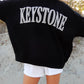 Person wearing a black sweatshirt with 'Keystone' printed on it, standing outdoors.
