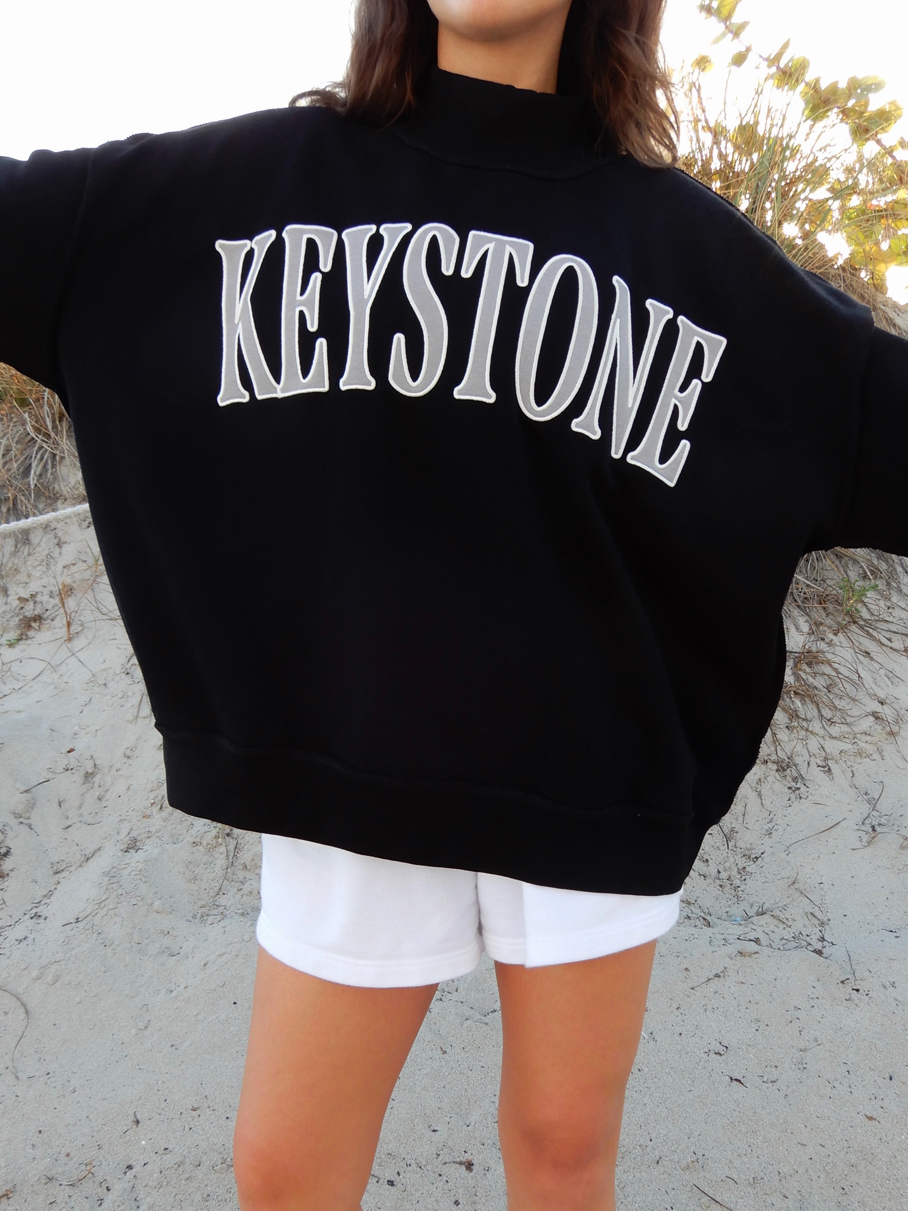 Person wearing a black sweatshirt with 'Keystone' printed on it, standing outdoors.