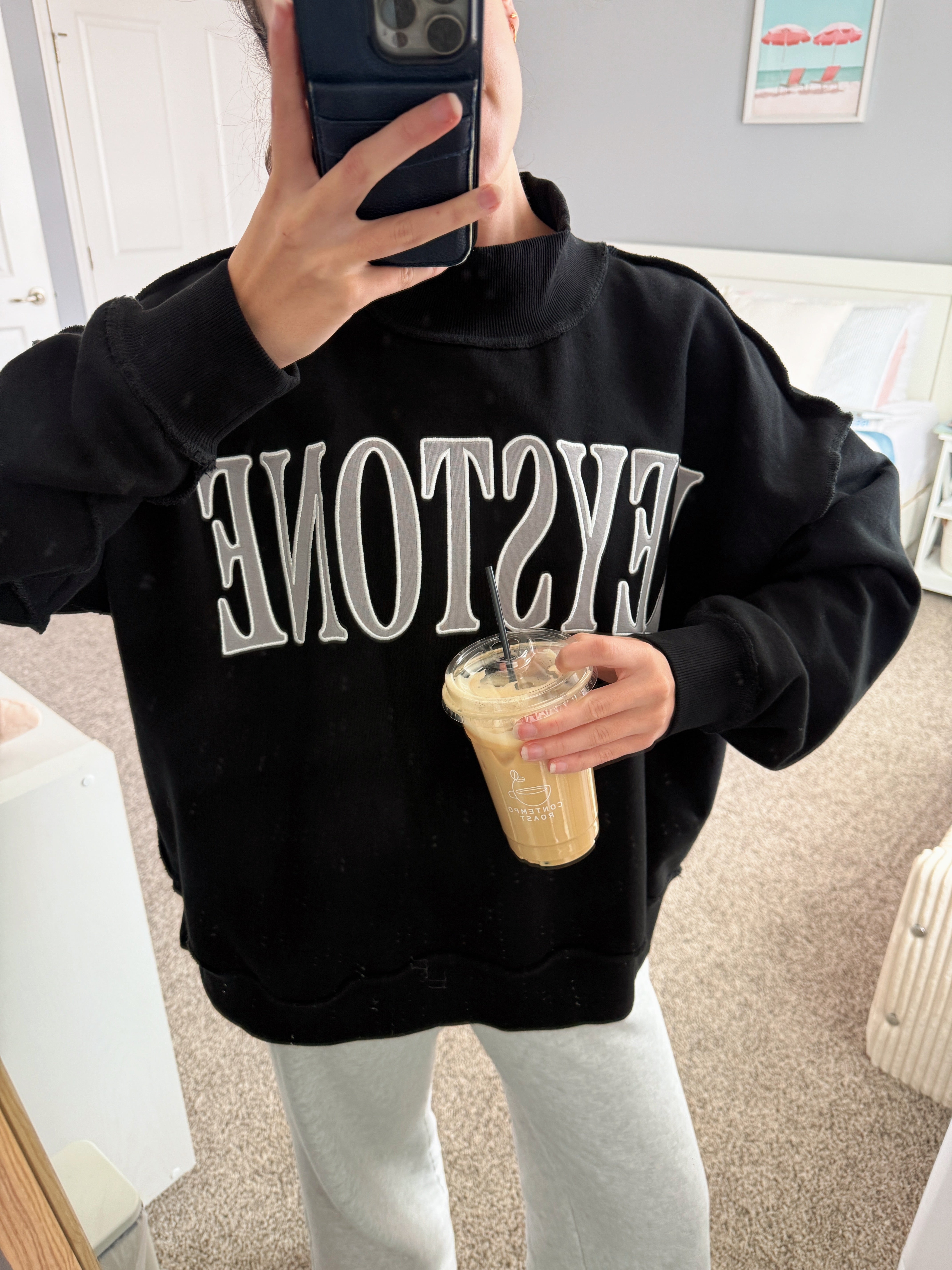 Person wearing a black sweatshirt with 'KEYSTONE' text, holding a drink.