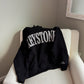 Black sweatshirt with 'Keystone' text on a white chair against a gray wall.