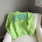 Green sweatshirt with 'Keystone' text on a white chair against a gray wall.