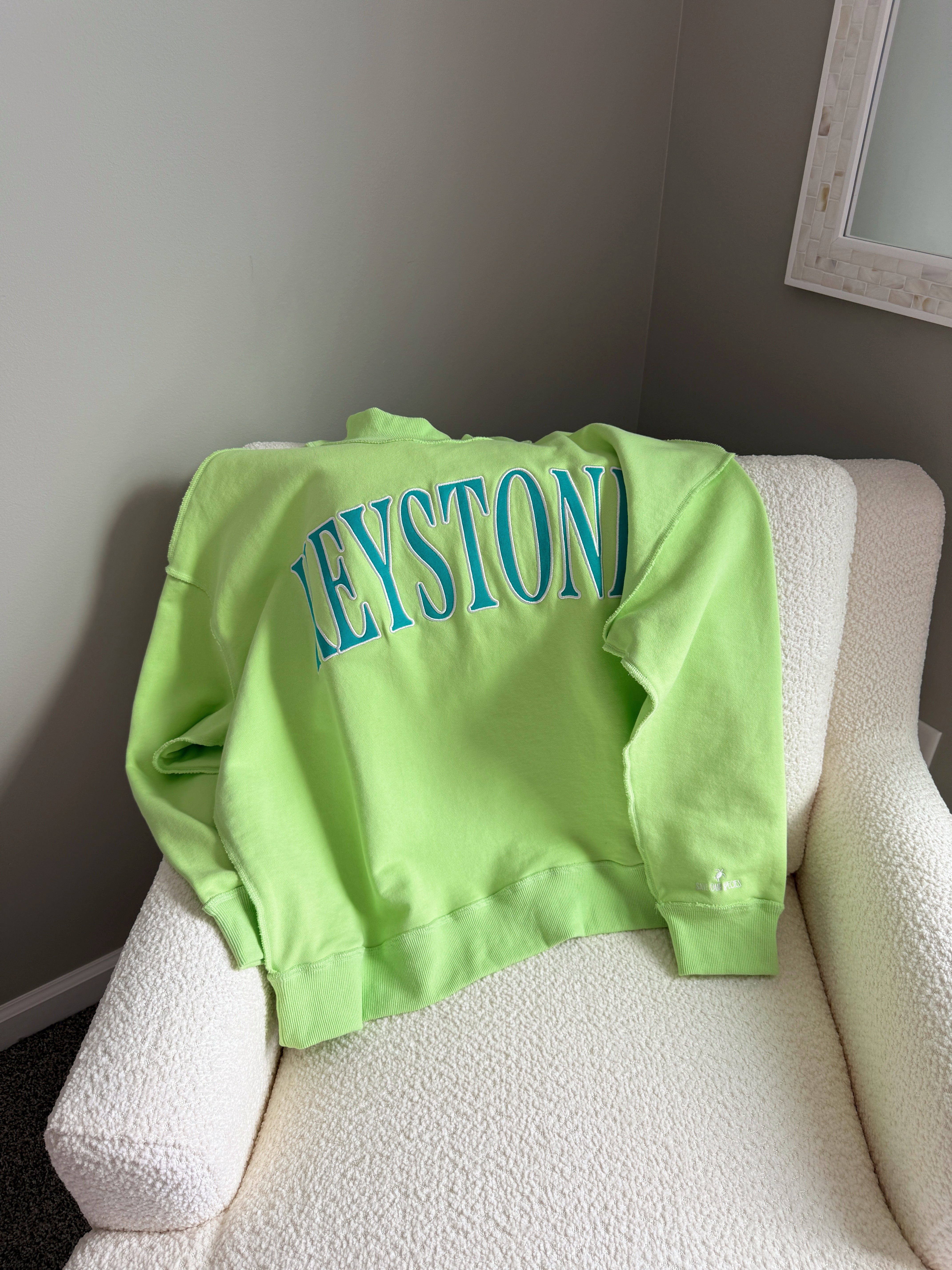 Green sweatshirt with 'Keystone' text on a white chair against a gray wall.