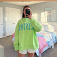 Person wearing a bright green sweatshirt with text in a bedroom.