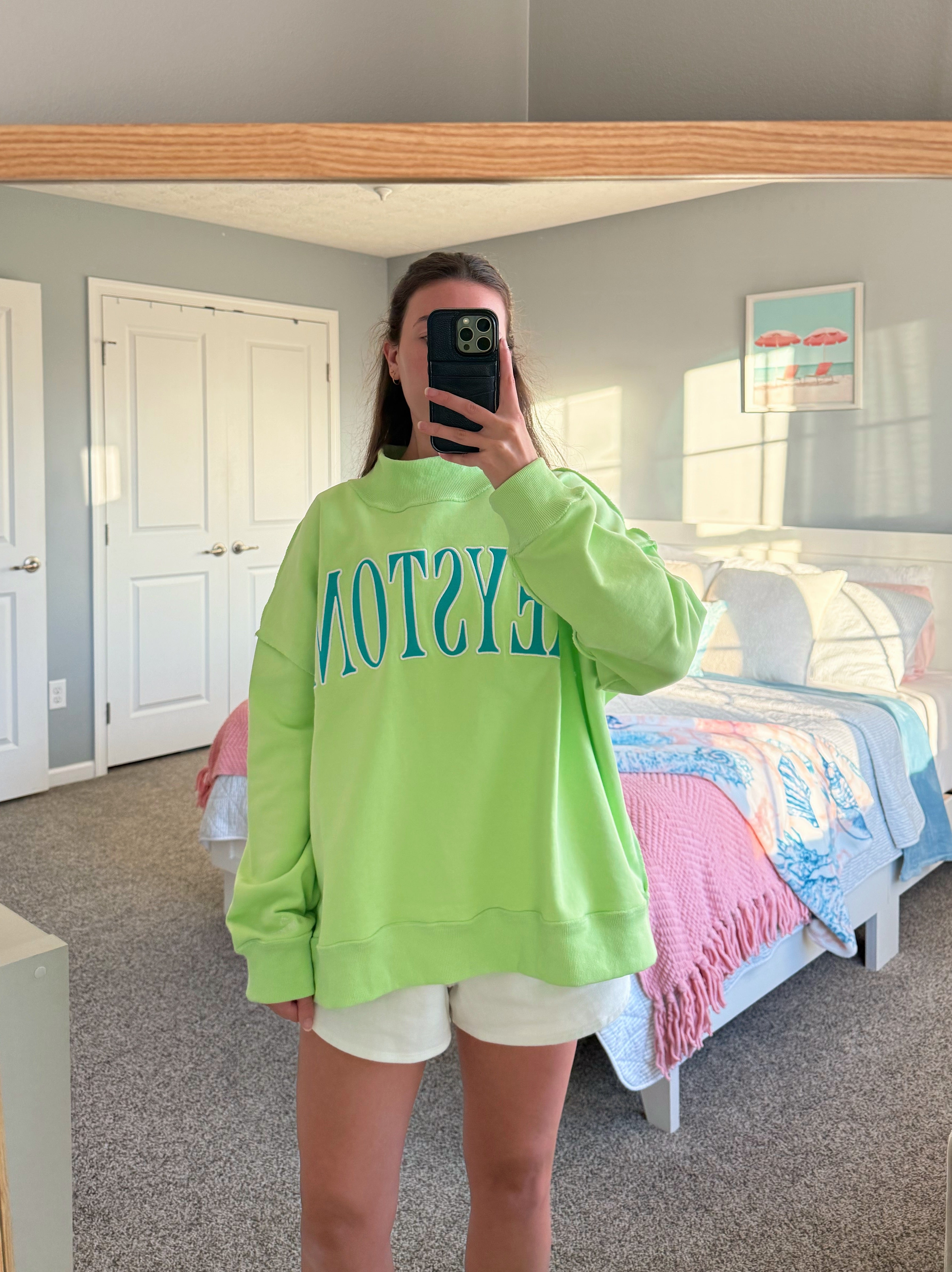 Person wearing a bright green sweatshirt with text in a bedroom.