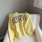 Yellow sweatshirt with 'KEYSTONE' text on a white chair against a gray wall.