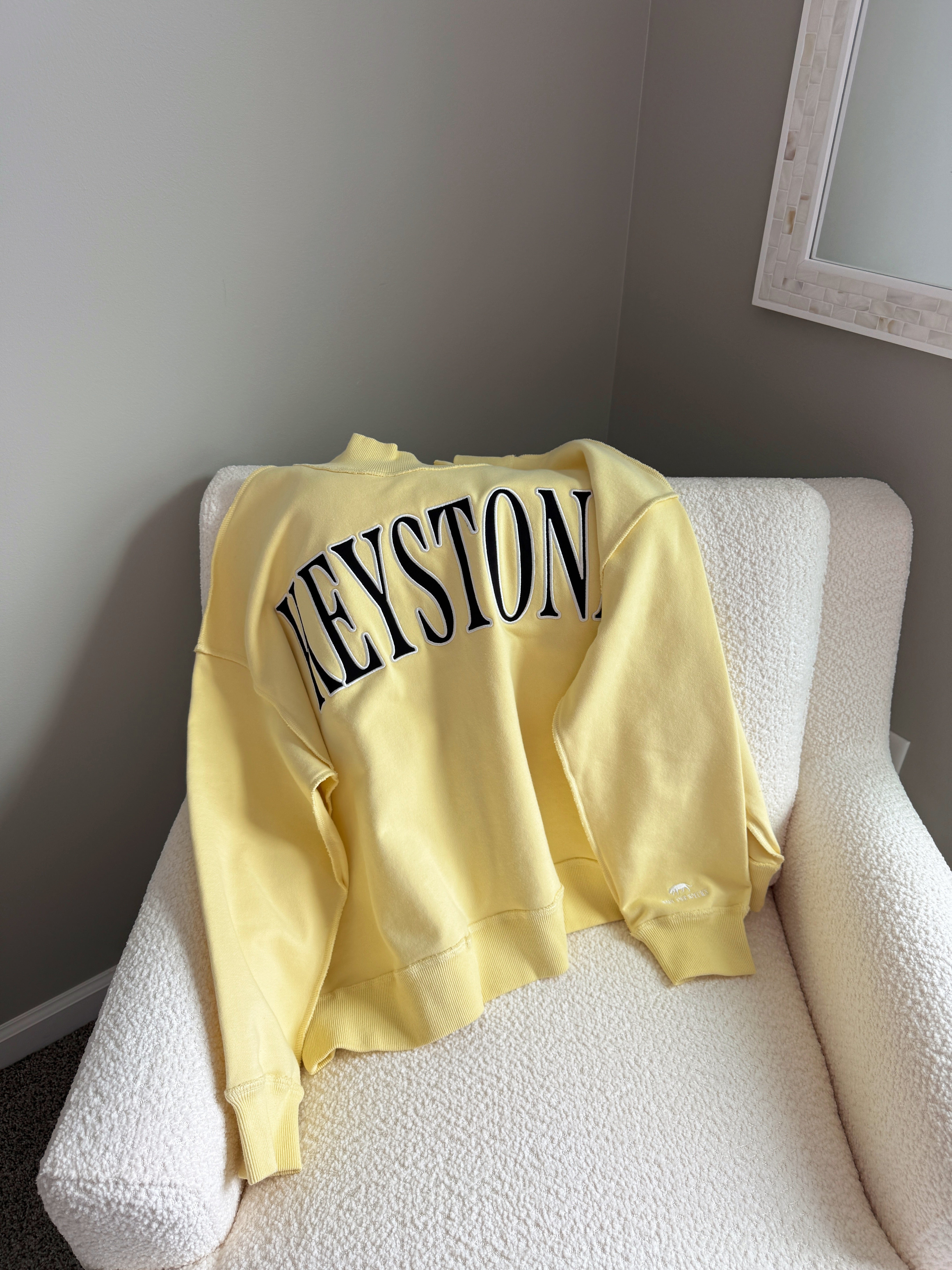 Yellow sweatshirt with 'KEYSTONE' text on a white chair against a gray wall.