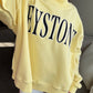 Person wearing a yellow sweatshirt with 'KEYSTONE' printed on it, sitting on a couch.