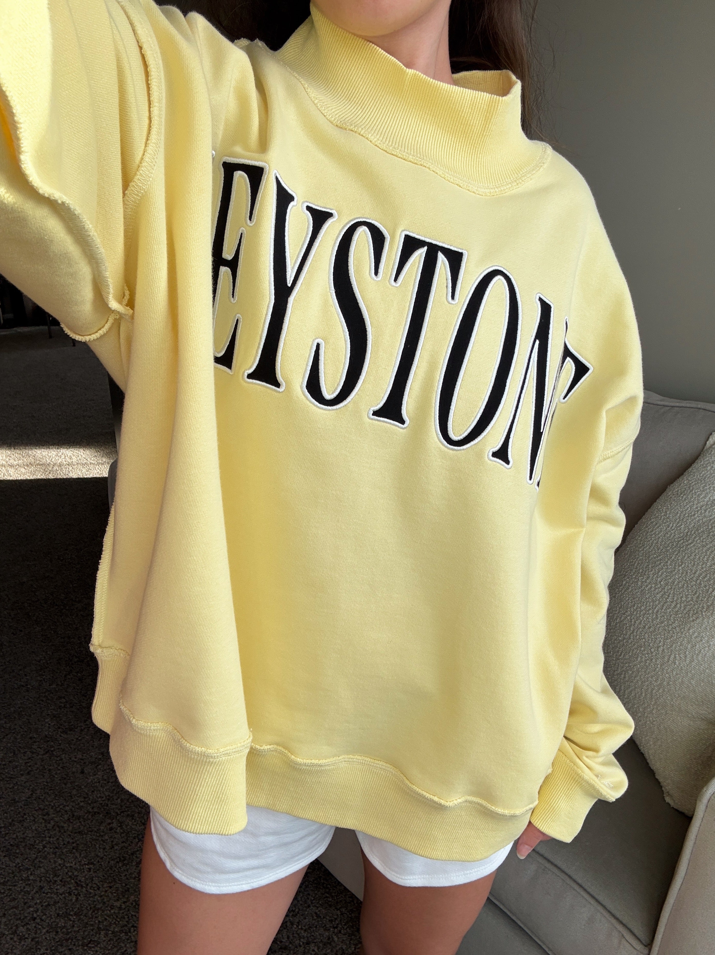 Person wearing a yellow sweatshirt with 'KEYSTONE' printed on it, sitting on a couch.