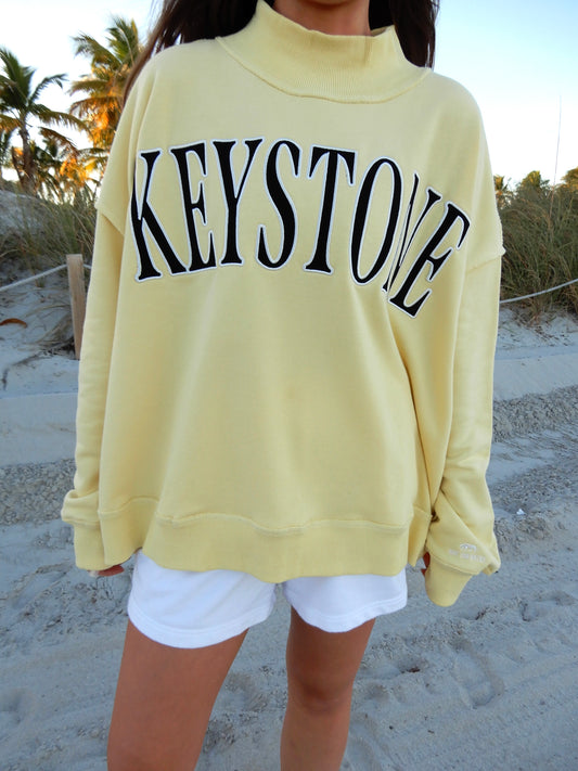 Person wearing a yellow sweatshirt with 'KEYSTONE' text on a beach.