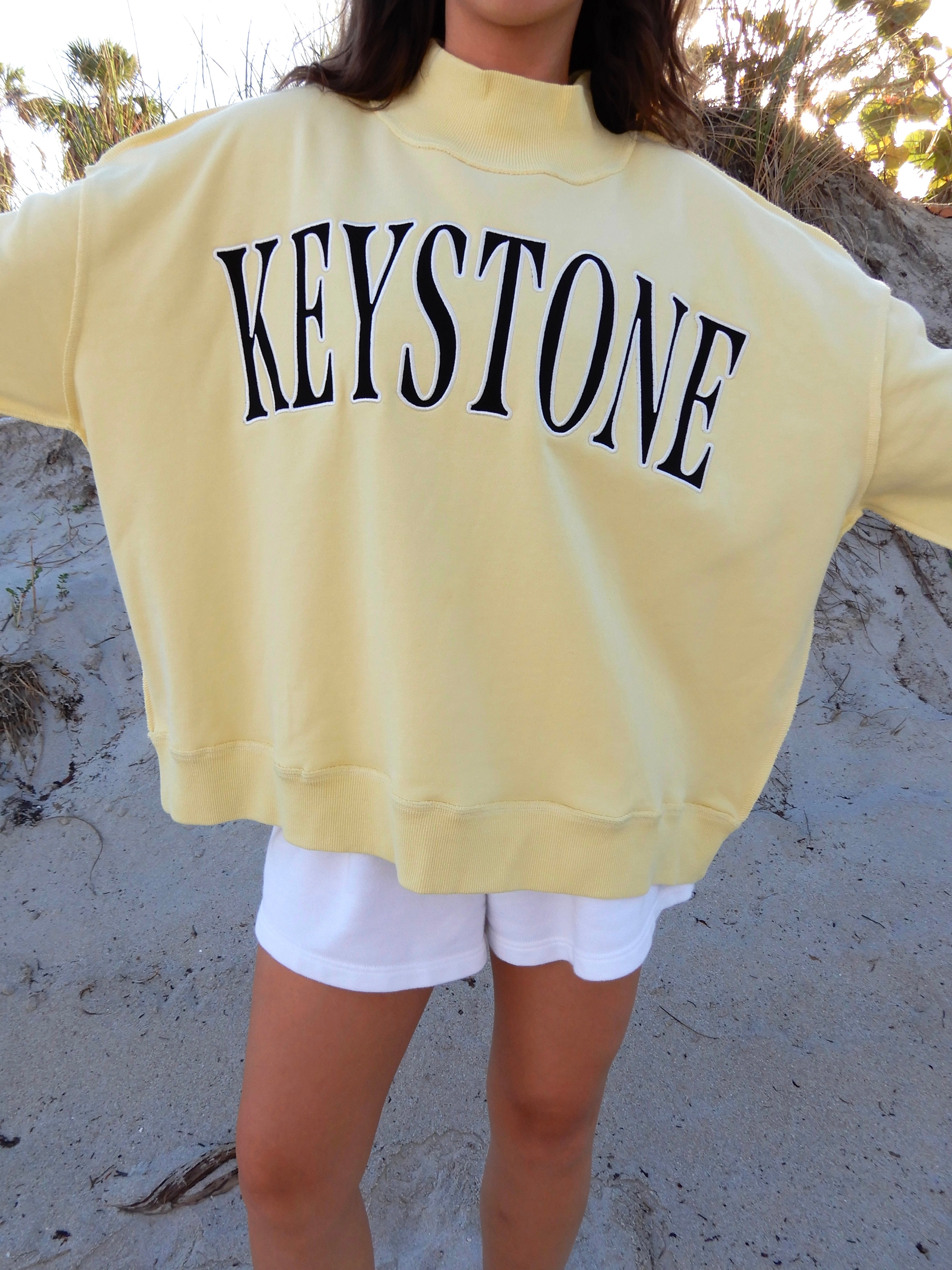 Person wearing a yellow sweatshirt with 'Keystone' printed on it, standing on sandy ground.