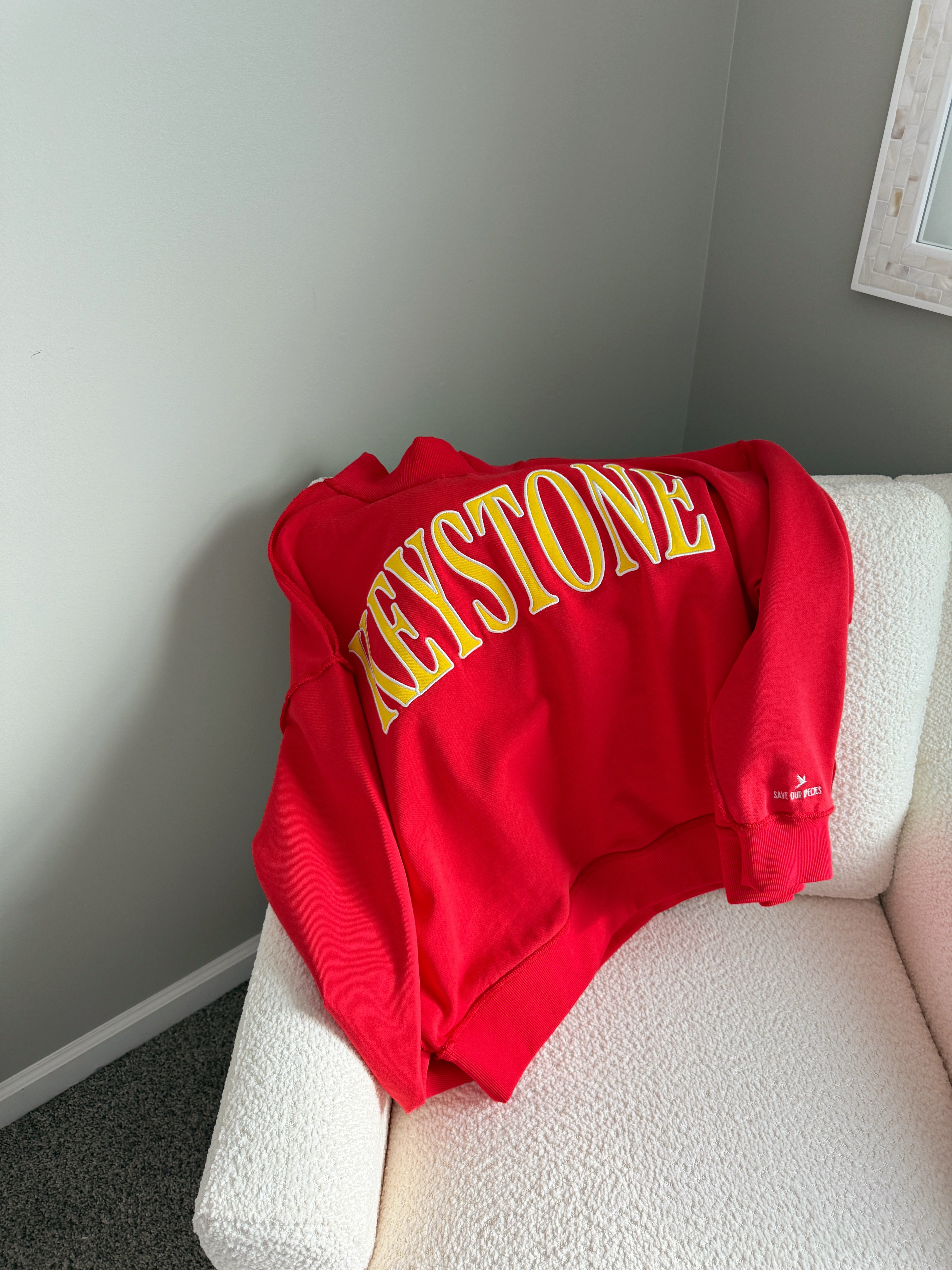 Red sweatshirt with yellow 'Keystone' text on a white couch against a gray wall.