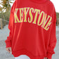 Person wearing a red sweatshirt with 'Keystone' printed in yellow on a beach.