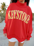 Person wearing a red sweatshirt with 'Keystone' printed in yellow on a beach.
