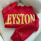 Red sweatshirt with yellow 'Keystone' text on a white couch