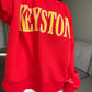 Red sweatshirt with yellow 'Keystone' text on a model in front of a couch